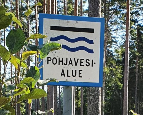 kyltti, jossa pohjavesialueen merkki, taustalla metsää.